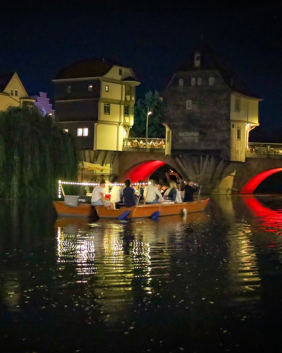 Beleuchtetes Funzelboot mit Lichterkette unter den Brückenhäusern von Bad Kreuznach bei Nacht